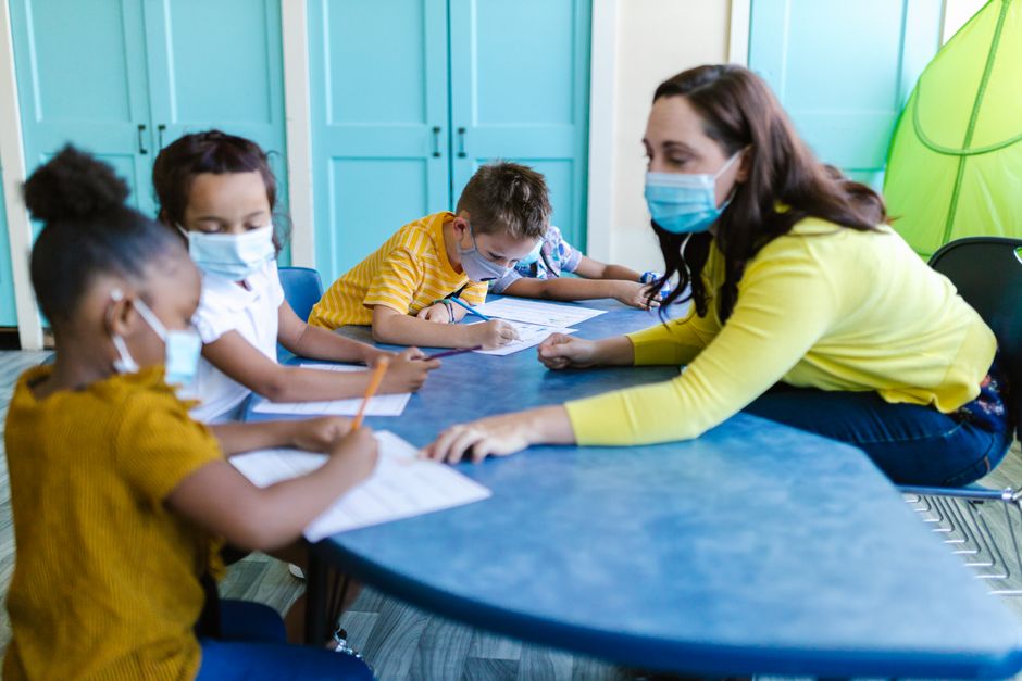 Teacher and children wearing masks engage in a classroom activity