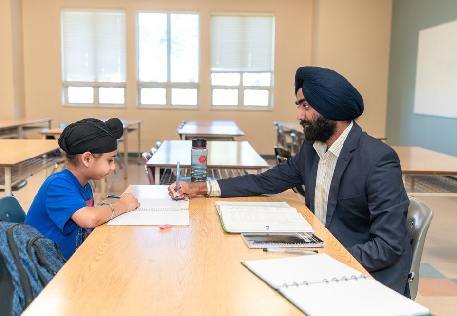 Male teacher helping a young student with studies in a classroom environment.